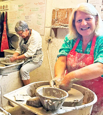 A lady makes a clay pot on a potters wheel