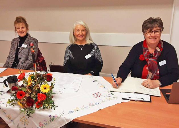 Three ladies sit at a table ready to chair the meeting