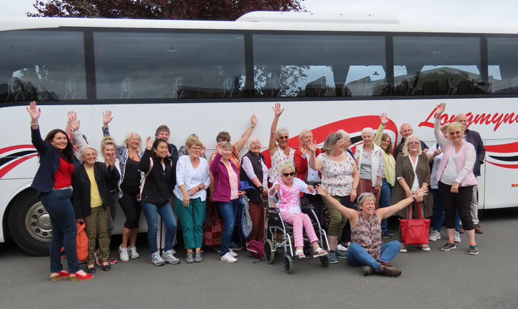 A group of ladies pose and wave in front of a coach
